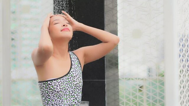 Attractive long-hair asian girl in swimsuits stand ender the shower slow motion