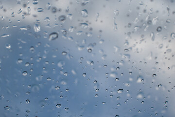 Raindrops on the window pane. Dew or condensation texture on a window against a blue sky. Selective focus on raindrops.