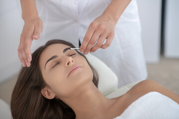 Dark-haired woman having procedure of eyebrows dying