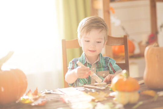 Happy Halloween concept. Cute little happy boy carving a pumpkin and decorated cookies for halloween on table indoors.