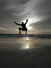 Fototapeta premium Sunset in the beach with a men silhouette jumping with the arms open