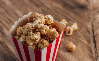 Red and white striped box with caramel popcorn on wooden rustic background.