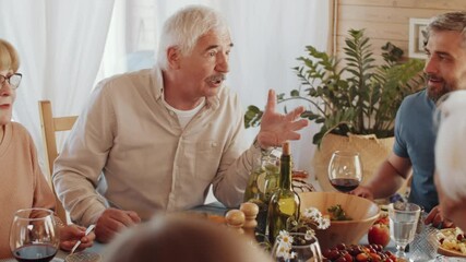 Senior man sitting at table and telling about something to cheerful family members during holiday dinner at home