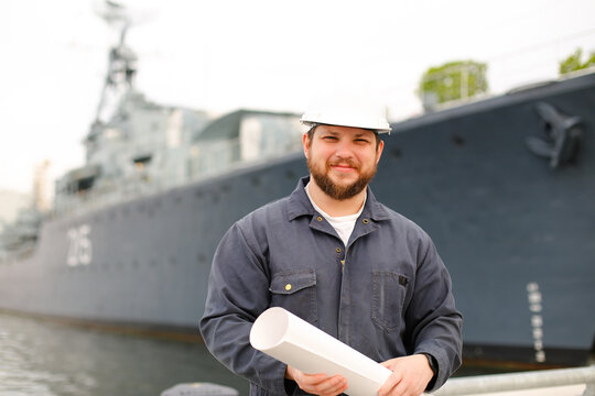 Marine chies officer holding blueprints and standing near vessel.