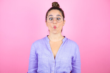 Young beautiful woman wearing glasses over isolated pink background making fish face with lips, crazy and comical gesture.