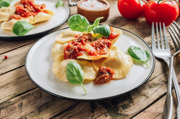Italian ravioli with meat tomato sauce and basil leaves with on a white dishes on an old rustic background.