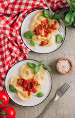 Italian ravioli with meat tomato sauce and basil leaves with on a white dishes on concrete background.