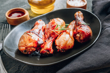 Chicken legs on black plate with red sauce and rosemary on black rustic background.