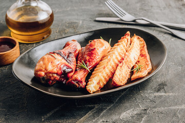 Chicken drumsticks with french fries on black plate on rustic black background.