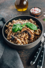 Original italian risotto with mushrooms and parmesan cheese in a dark bowl on a dark background.