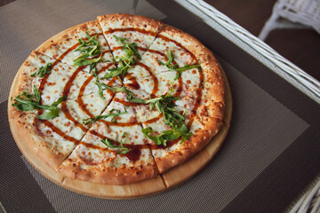 Pizza with arugula on a wooden plate on grey background in summer terrace