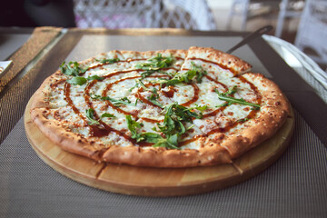Pizza with arugula on a wooden plate on grey background in summer terrace