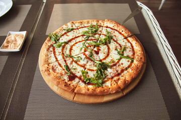 Pizza with arugula on a wooden plate on grey background in summer terrace