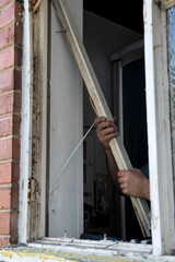 Hands of workman pulling part of old wooden window from out of brick wall during building renovations