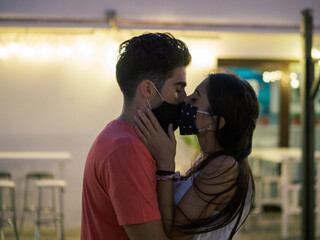 Beautiful kissing couple wearing medical masks on a romantic date - the new normal due to Covid-19