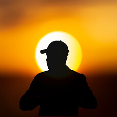 Silhouette of traveler in baseball cap on sunset sun background