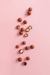 Flat lay composition with cracked macadamia nuts on pink background, top view with copyspace. Vertical photo