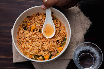 Tom Yum instant noodles in a white ceramic cup on a wooden floor