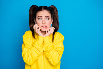 Photo of pretty lady two tails hairdo arms on cheekbones look fear side empty space made mistake uncomfortable situation wear yellow sweatshirt pullover isolated bright blue color background
