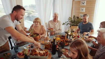 Cheerful man cutting roasted turkey for his family while hosting Thanksgiving holiday dinner at home - Powered by Adobe