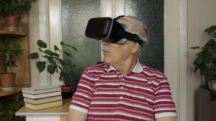 Fototapeta premium Senior grandfather man in virtual headset glasses watching 3d video in 360 vr helmet at home