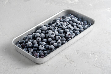 Frozen blueberries in a metal tray on a concrete background.