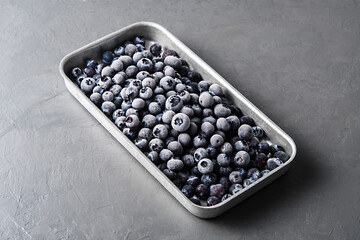 Frozen blueberries in a metal tray on a concrete background.