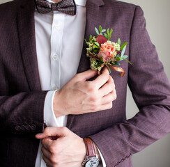a man in a wedding suit adjusts a boutonniere
