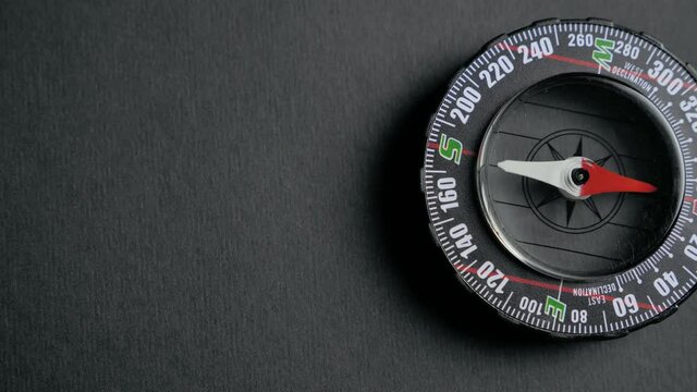 a modern compass lying on a black desk with a red arrow that shows the direction. Concept of travel, adventure, expedition, business, choice and possibilities. 4k