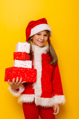 Little girl wearing Santa Claus costume holding bunch of Christmas presents