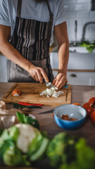 Obraz na płótnie Canvas Handsome Man Chopping a Green Spring Onion with a Sharp Kitchen Knife. Man in White Shirt and Apron is Making a Organic Salad Meal in a Modern Sunny Kitchen. Natural Clean Diet and Healthy Lifestyle.