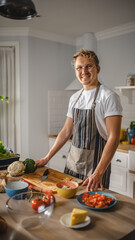Handsome Man in White Shirt and Apron is Making a Healthy Organic Salad Meal in a Modern Sunny Kitchen. Hipster Man in Glasses Smiles at the Camera. Natural Clean Diet and Healthy Way of Life Concept.