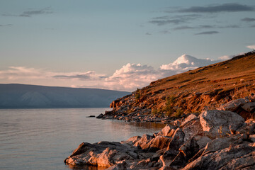 Orange big stones in the light of the setting sun, by the bay with the shore, coast on lake Baikal