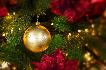 Golden decorative ball hanging on a branch of a Christmas tree in the light of garland. Phot backdrop decoration for Christmas design. Festive banner postcard flyer copy space