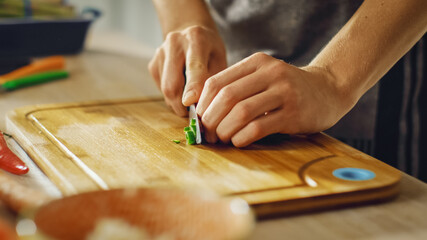 Obraz premium Close Up Shot of a Man Chopping a Green Chili Pepper with a Sharp Kitchen Knife. Preparing a Healthy Organic Salad Meal in a Modern Kitchen. Natural Clean Diet and Healthy Way of Life Concept.