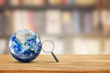 Learning and Education Concept : Magnifying glass lean on blue planet earth with blurry image of library room in background. (Elements of this image furnished by NASA.)