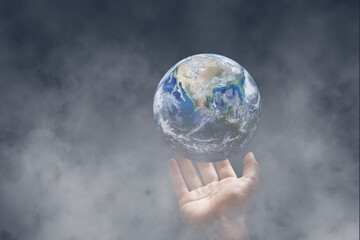 Hand holding blue planet earth in dark room with white smoke. (Elements of this image furnished by NASA.)