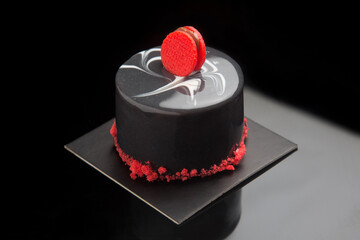 Individual cake with black mirror glaze, on black background.