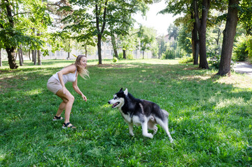 Naklejka na ściany i meble young beautiful girl runs with a husky in the park. The blonde plays with the dog.