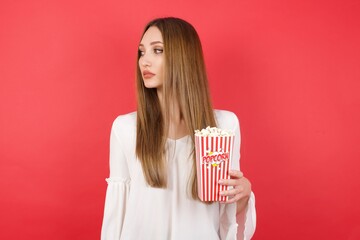 Close up side profile photo Eastern European woman holding bucket with popcorn standing over isolated red background ready to have a walk.