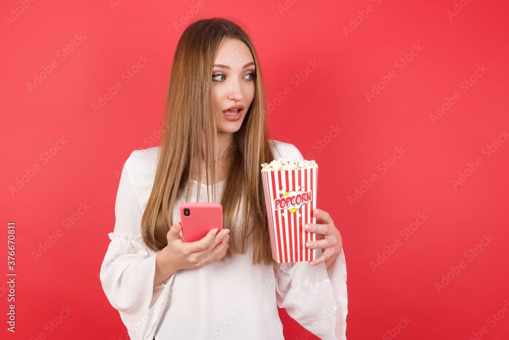 Wall mural copyspace photo of eastern european woman holding bucket with popcorn standing over isolated red bac