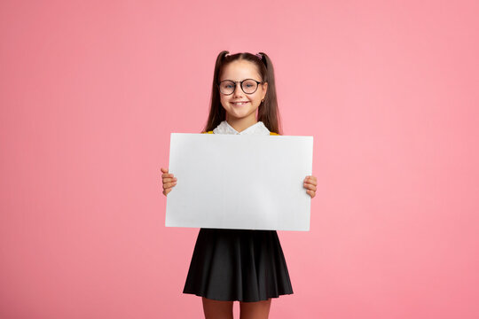 Cheerful child schoolgirl in uniform and glasses holds sign with empty space