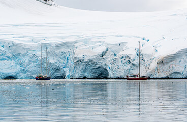 Antarctica, Antarctic Peninsula. In the Gerlach Street. Fournier Bay. Sailing boats arounded by ice floes with the enormous Ice shelf in the background. February 2020