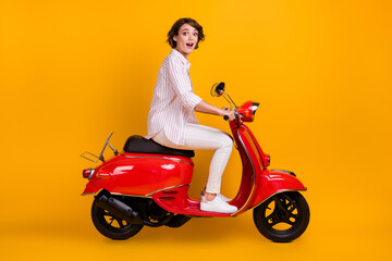 Fototapeta na wymiar Side profile full length photo of charming young lady riding motorcycle enjoying traveling unexpected town roads wear white striped shirt pants isolated yellow bright color background