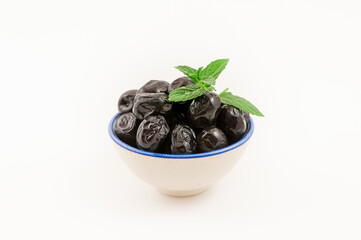 Oily black olives and fresh mint leaves in a small porcelain bowl, isolated on white background