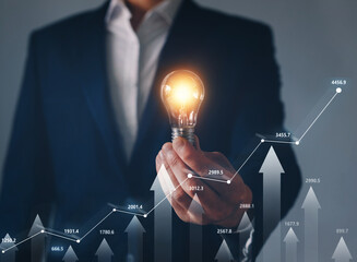 Businessman holding illuminated lightbulb with forex trading and financial market . Concept of...