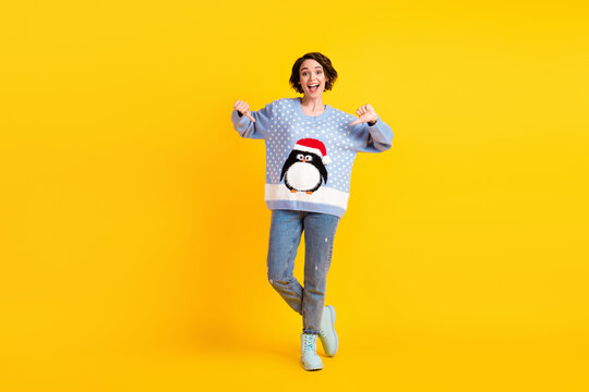 Full size photo of pretty charming lady x-mas party direct fingers showing friends new jumper funky cute fluffy penguin wear ugly ornament sweater jeans boots isolated yellow color background