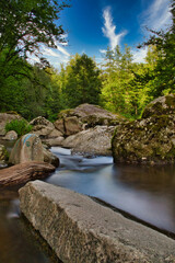 Naklejka na ściany i meble Landschaftsaufnahme eines Flusses mit grossen Steinen im Wald mit Langzeitbelichtung