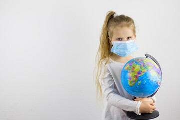 A sad child looks at the camera in a protective mask and holds a globe. The concept of isolating the world from a new generation virus