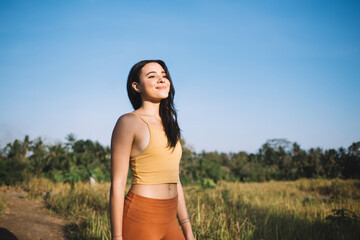 Positive slim beautiful woman enjoying training on nature field on sunny day enjoying relaxation, smiling caucasian girl inspiring with meadow resting and feeling body vitality for healthy body